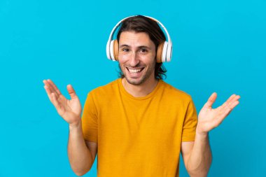 Mavi arka planda izole genç yakışıklı adam şaşırdı ve müzik dinliyor