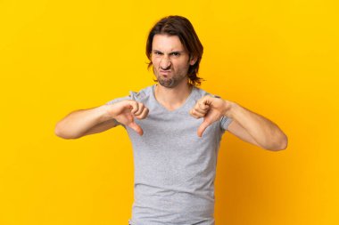 Sarı arka planda iki eliyle baş parmağını gösteren genç ve yakışıklı bir adam.