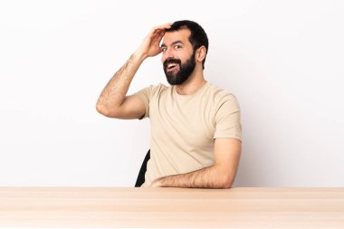 Masada sakallı beyaz bir adam yan tarafa bakarken sürpriz jest yapıyor..