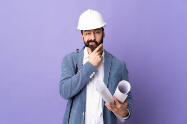 Miğferli genç bir mimar, izole edilmiş mor arka plan üzerinde planlar tutuyor.