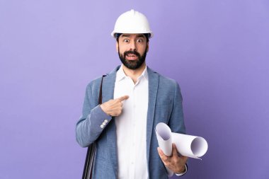 Miğferli genç bir mimar, izole edilmiş mor arkaplanının planlarını tutuyor.