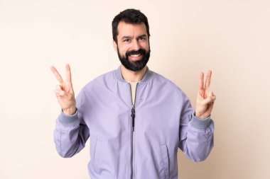 Sakallı, ceketli beyaz bir adam izole edilmiş arka planda zafer işaretini iki eliyle gösteriyor.