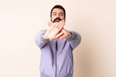 Sakallı, ceketli beyaz bir adam izole edilmiş bir arka planda, bir eylemi durdurmak için el hareketi yapıyor.