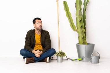 Bahçıvan içeride yerde oturuyor. Kafası karışıkken yukarı bakıyor.