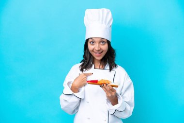 Mavi arka planda Sashimi tutan genç İspanyol aşçı kadın. Şaşırtıcı bir yüz ifadesi var.