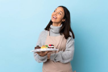Pasta şefi mavi arka planda büyük bir pasta tutuyor. Mutlu ve gülümsüyor..