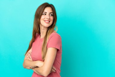 Mavi arka planda soyutlanmış genç beyaz kadın yana bakıyor ve gülümsüyor.