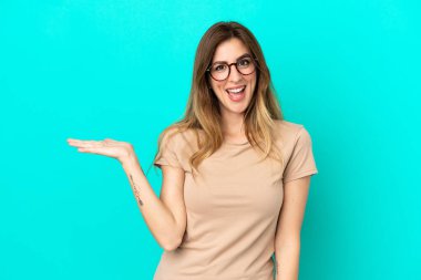 Mavi arka planda izole edilmiş genç beyaz kadın bir ilan vermek için avucunun içinde hayali bir fotokopi makinesi tutuyor.