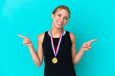 Mavi arka planda madalyaları olan beyaz genç bir kadın parmak uçlarını işaret ediyor ve mutlu.
