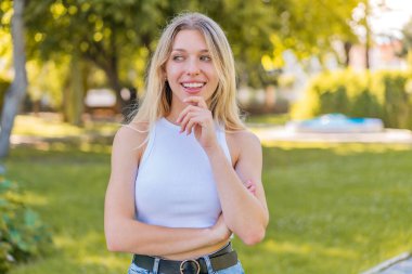 Açık havada genç sarışın kadın yan tarafa bakıyor.