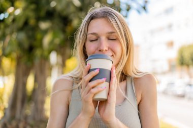 Açık havada elinde kahve tutan genç sarışın kadın.