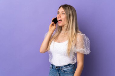 Mor arka planda izole edilmiş genç sarışın kadın cep telefonuyla sohbet ediyor.