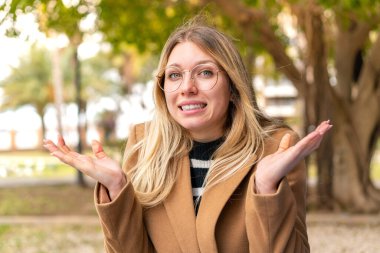 Dışarıda el kaldırırken kuşkuları olan güzel sarışın bir kadın.