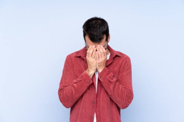 Mavi arka planda kadife ceket giyen genç beyaz adam yorgun ve hasta bir ifade takınıyor.