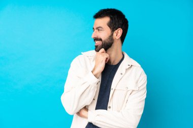 Mavi arka planda beyaz kadife ceketli yakışıklı genç adam yan tarafa bakıyor.