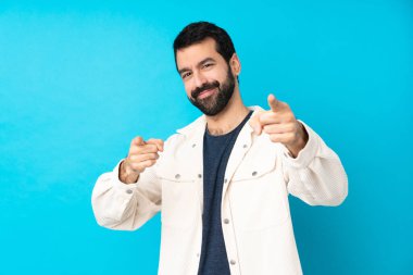 Mavi arka plan üzerinde beyaz kadife ceketli genç ve yakışıklı bir adam gülümserken sana işaret ediyor.