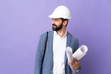 Miğferli genç bir mimar, elinde yalıtılmış mor arka plan planları var.