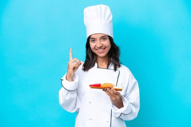 Mavi arka planda saşimi tutan genç İspanyol aşçı kadın harika bir fikre işaret ediyor.