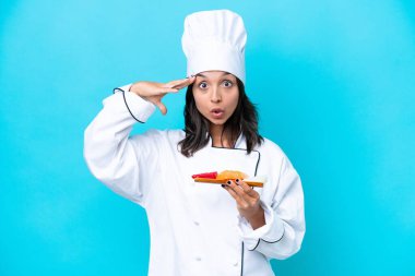 Genç İspanyol aşçı kadın elinde sashimi tutarken mavi arka planda sürpriz bir ifadeyle