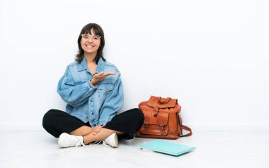 Beyaz arka planda izole bir zeminde oturan genç bayan bir fikir sunuyor ve gülümsüyor.