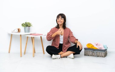 Genç melez kadın, beyaz arka planda soyutlanmış bir şekilde yerde oturmuş giysilerini katlıyor.