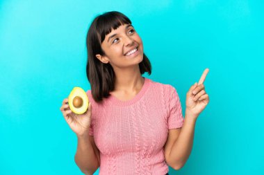 Mavi arka planda avakado tutan genç melez kadın harika bir fikre işaret ediyor.