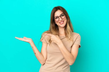 Mavi arka planda izole edilmiş genç beyaz kadın bir ilan vermek için avucunun içinde hayali bir fotokopi makinesi tutuyor.
