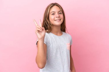 Little caucasian girl isolated on pink background smiling and showing victory sign