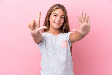 Pembe arka planda izole edilmiş küçük beyaz kız yediyi parmaklarıyla sayıyor.