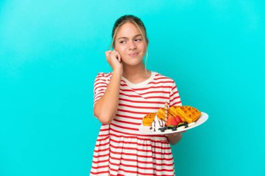 Mavi arka planda gözleme tutan küçük beyaz kız hayal kırıklığına uğramış ve kulaklarını kapatmış.