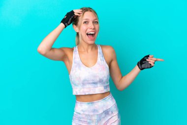 Mavi arka planda izole edilmiş beyaz kadın. Şaşırmış ve işaret ediyor.