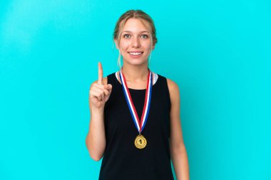 Mavi arka planda madalyaları olan beyaz genç bir kadın en iyinin işareti olarak parmağını kaldırıyor.