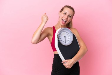 Pembe arka planda, tartı makinesiyle izole edilmiş beyaz bir kadın zafer jesti yapıyor.