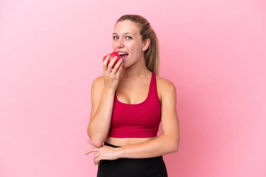 Pembe arka planda izole edilmiş beyaz bir kadın elma yiyor.