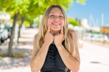 Açık havada gülümseyen mutlu ve hoş bir ifadeyle genç sarışın kadın.