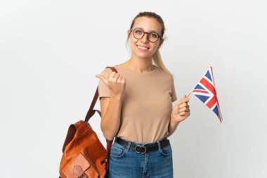 Beyaz arka planda izole edilmiş bir Birleşik Krallık bayrağı taşıyan genç sarışın kadın bir ürünü sunmak için kenarı işaret ediyor.