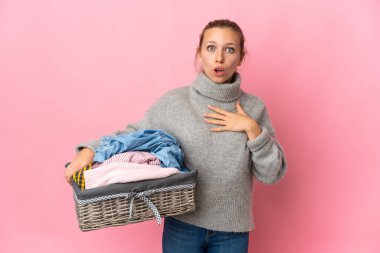 Pembe arka planda izole edilmiş çamaşır sepetini tutan genç bir kadın sağa bakarken şaşırmış ve şok olmuştu.