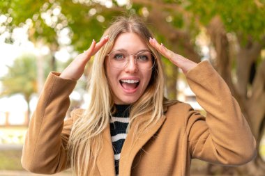 Genç, güzel, sarışın bir kadın açık havada, sürpriz bir ifadeyle.