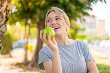 Genç sarışın kadın açık havada elmalı ve mutlu.