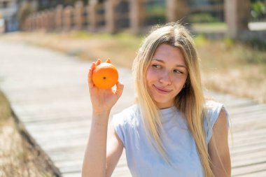 Açık havada elinde portakal tutan genç sarışın kadın.