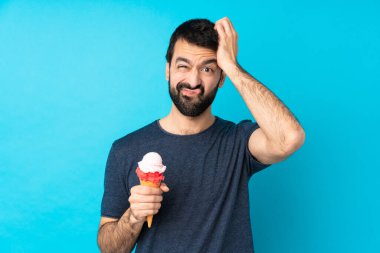 İzole edilmiş mavi arka planda kornet dondurması olan genç bir adam hayal kırıklığı ifadesi sergiliyor ve anlayamıyor.
