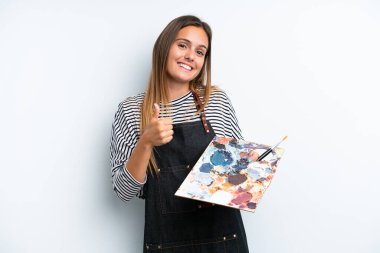 Beyaz arka planda izole edilmiş palet tutan beyaz bir kadın baş parmak hareketi yapıyor.