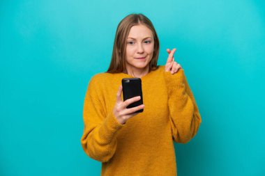 Mavi arka planda izole edilmiş genç Rus kadın parmakları çapraz cep telefonu kullanıyor.