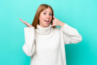 Genç kızıl saçlı kadın mavi arka planda izole edilmiş, telefon hareketlerinde şüpheli.