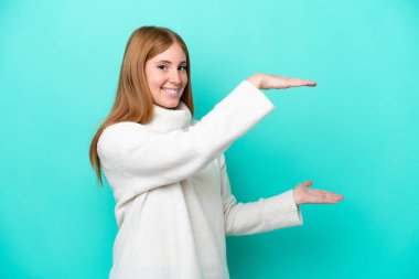 Genç kızıl saçlı kadın mavi arka planda izole edilmiş bir ilan vermek için kopyalama alanı tutuyor.