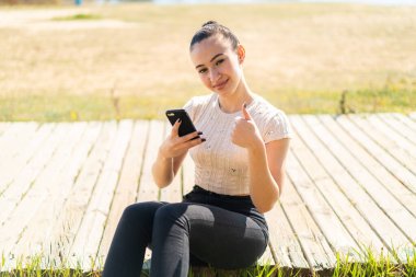 Dışarıdaki Faslı genç kız başparmak kaldırırken cep telefonu kullanıyor.