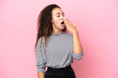 Pembe arka planda izole edilmiş genç İspanyol kadın esniyor ve ağzını eliyle açık tutuyor.