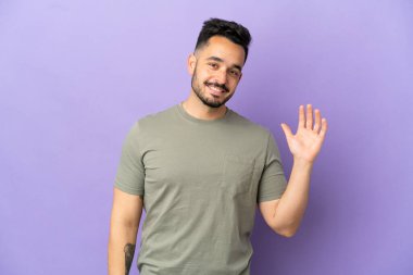 Mor arka planda izole edilmiş genç beyaz adam mutlu bir ifadeyle selamlıyor.