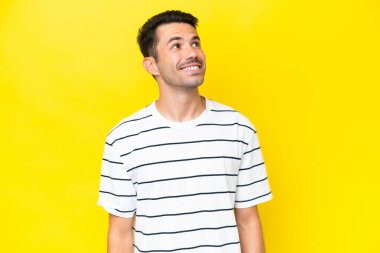 Soyutlanmış sarı arka planda genç yakışıklı bir adam yukarı bakarken bir fikir düşünüyor.