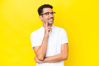 Soyutlanmış sarı arka planda genç yakışıklı bir adam yukarı bakarken bir fikir düşünüyor.